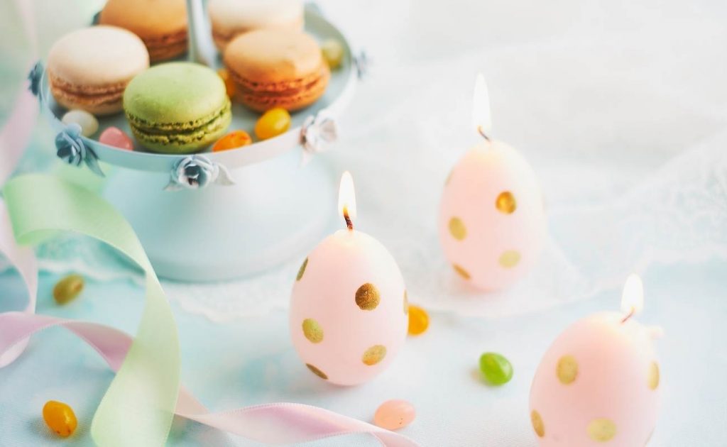 Velas de Pascua en una dorma de huevo con macarons de colores al lado.